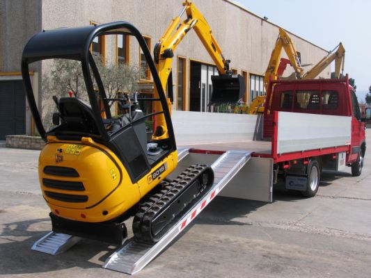 Mini digger montant des rampes posées sur plateau